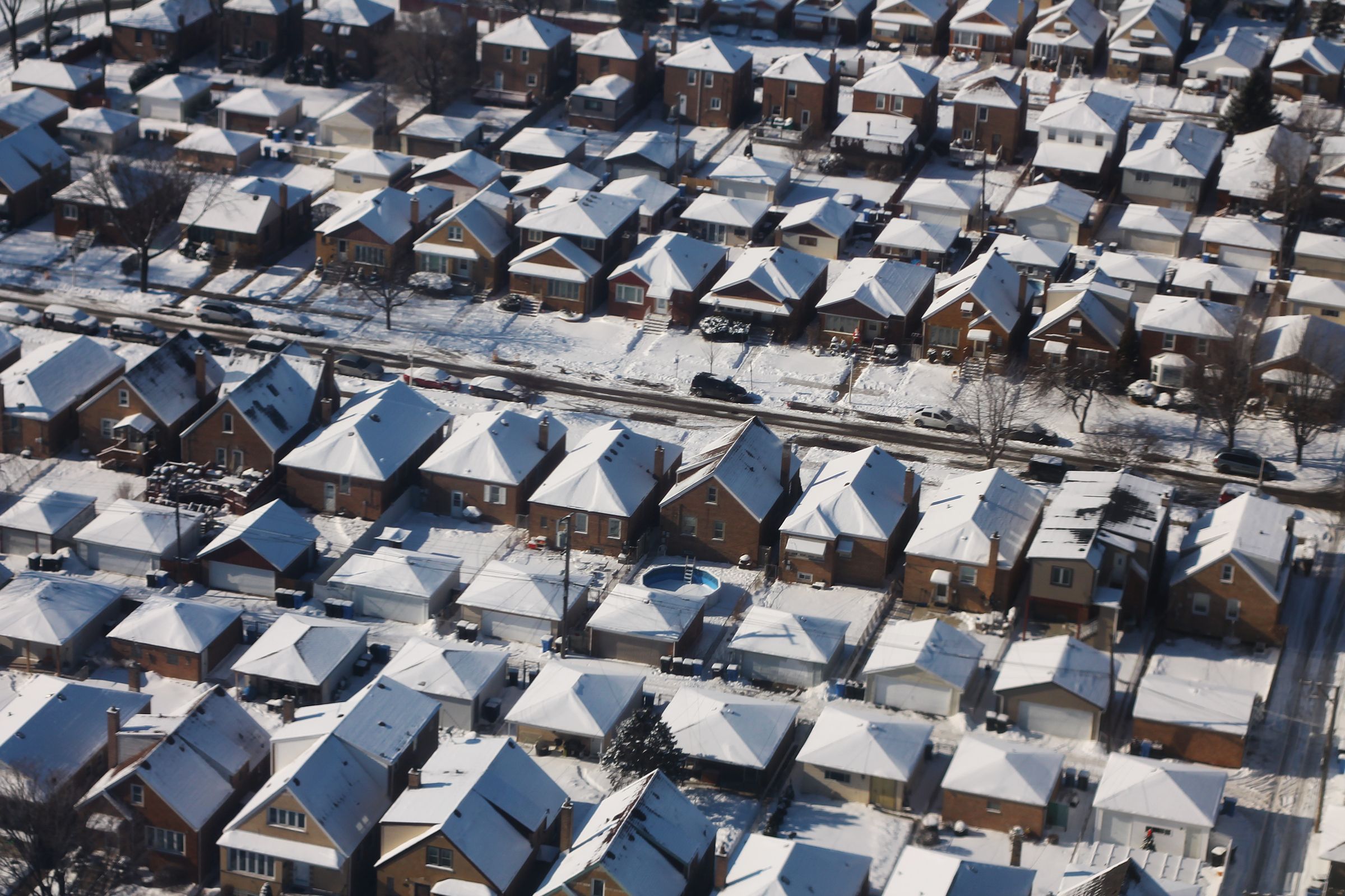 Rows of snow-covered Chicago bungalows and garages beside a cleared street, seen from the air.